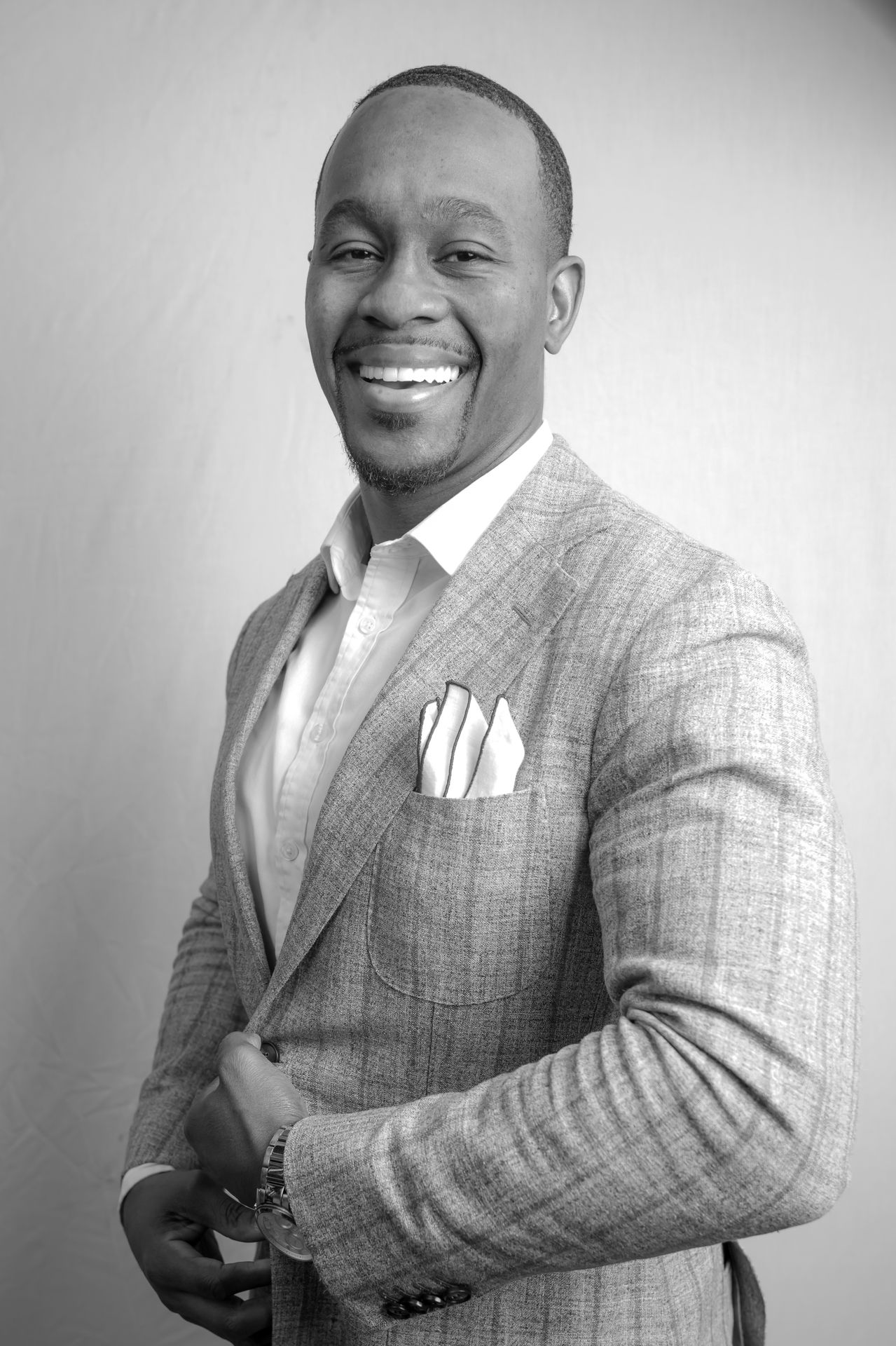Black-and-white portrait of a laughing man in a gray check blazer on a gray background
