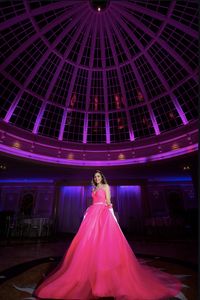 Quinceañera smiling in a pink gown beneath a purple-lit dome ceiling