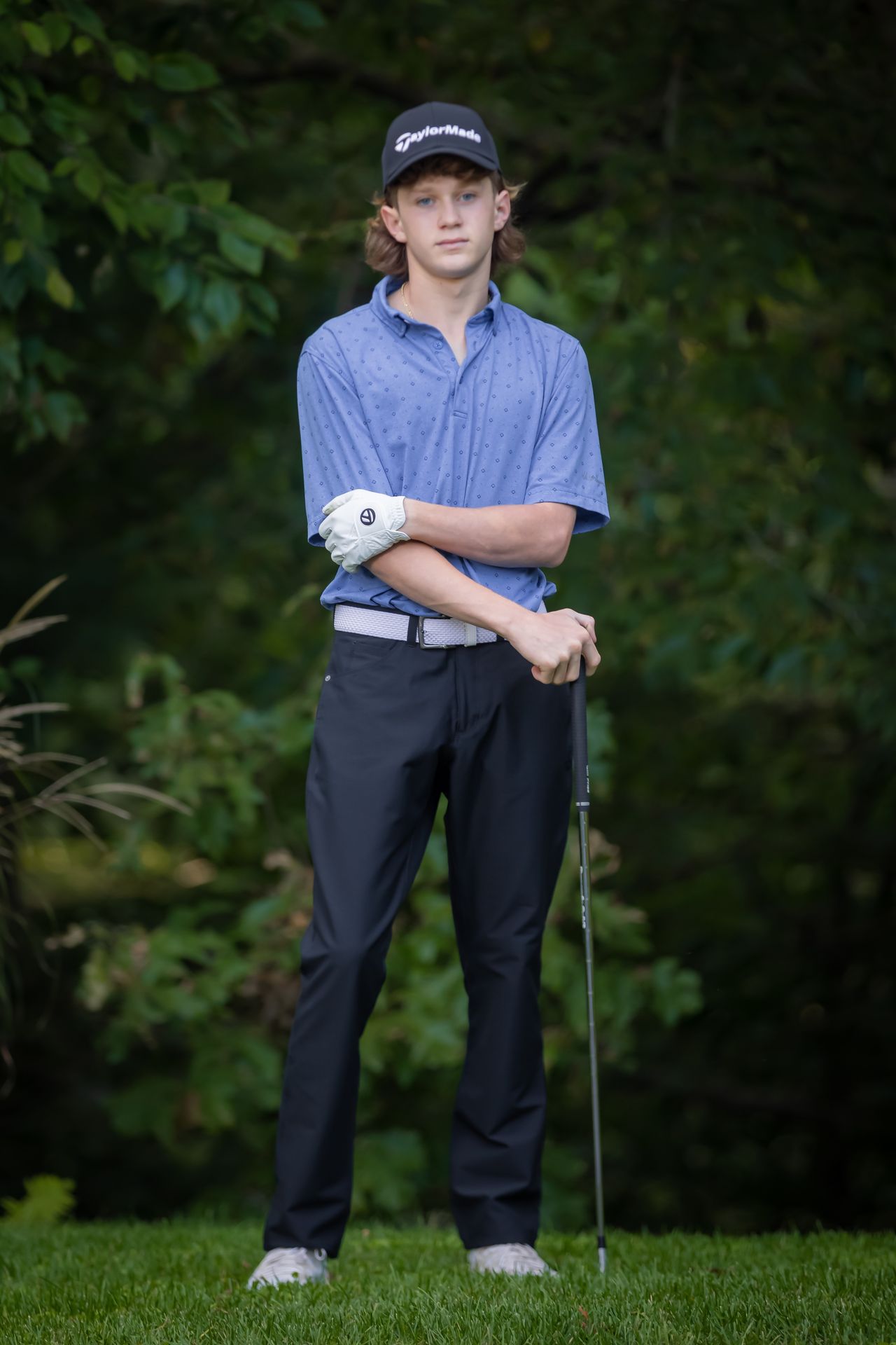 Young golfer in a blue polo shirt and cap standing with a club on a green