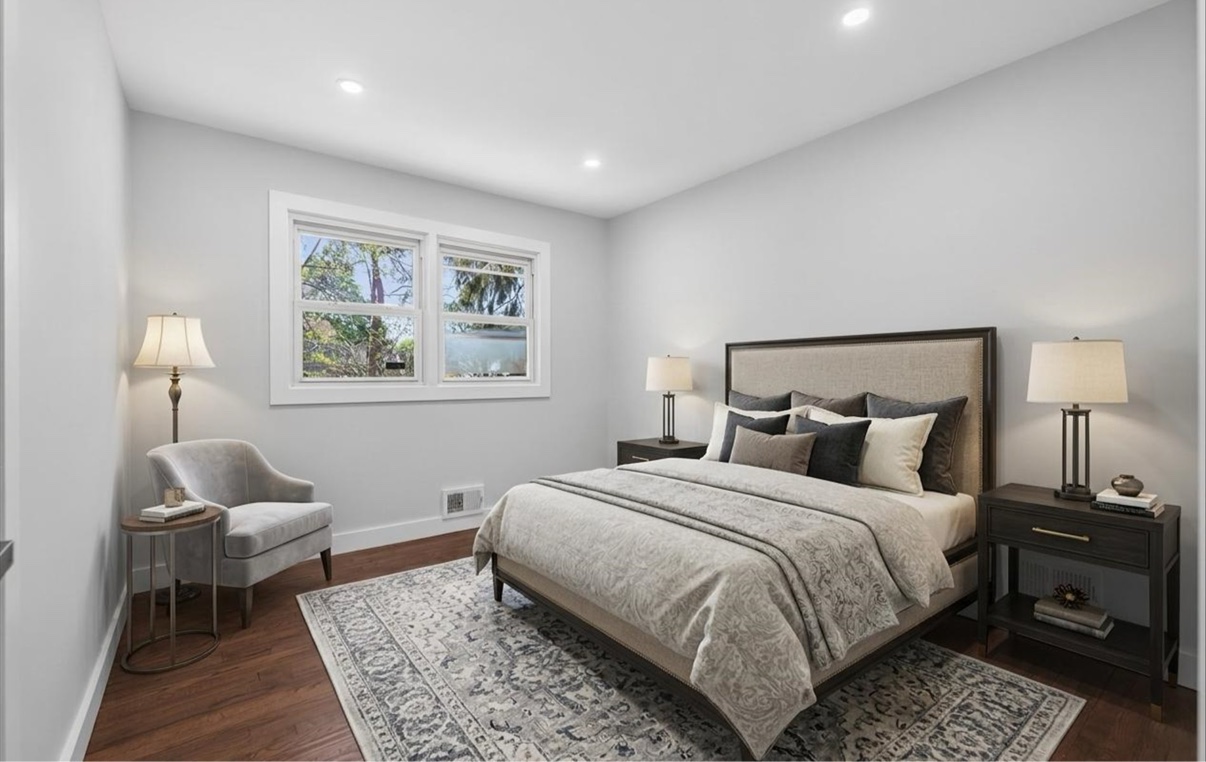 Staged bedroom with neutral bedding, an armchair and a bright window