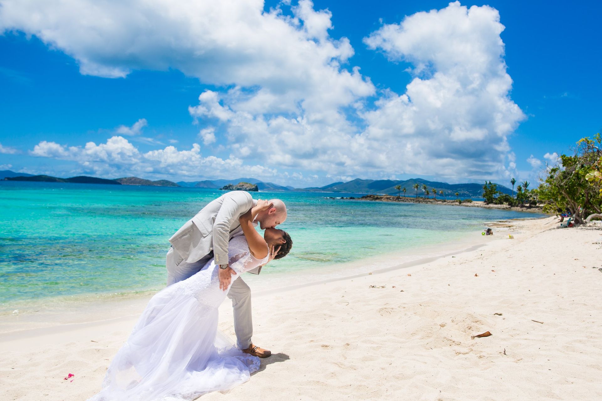 Groom dipping his bride on a beach under a bright blue sky