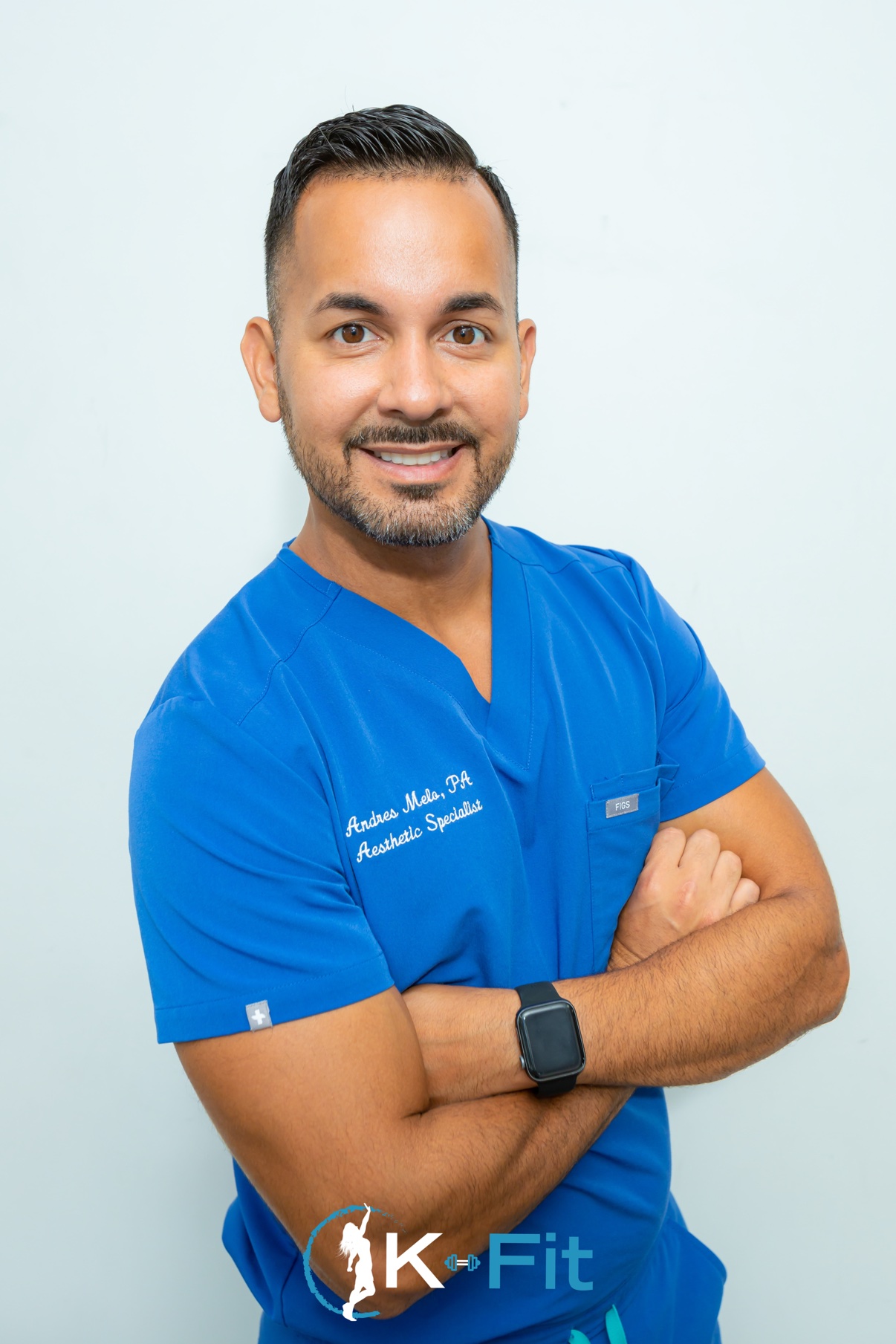 Smiling man in blue medical scrubs with crossed arms on a light background