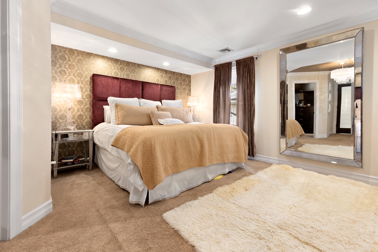 Bedroom with a burgundy upholstered headboard, damask wallpaper and a mirrored frame