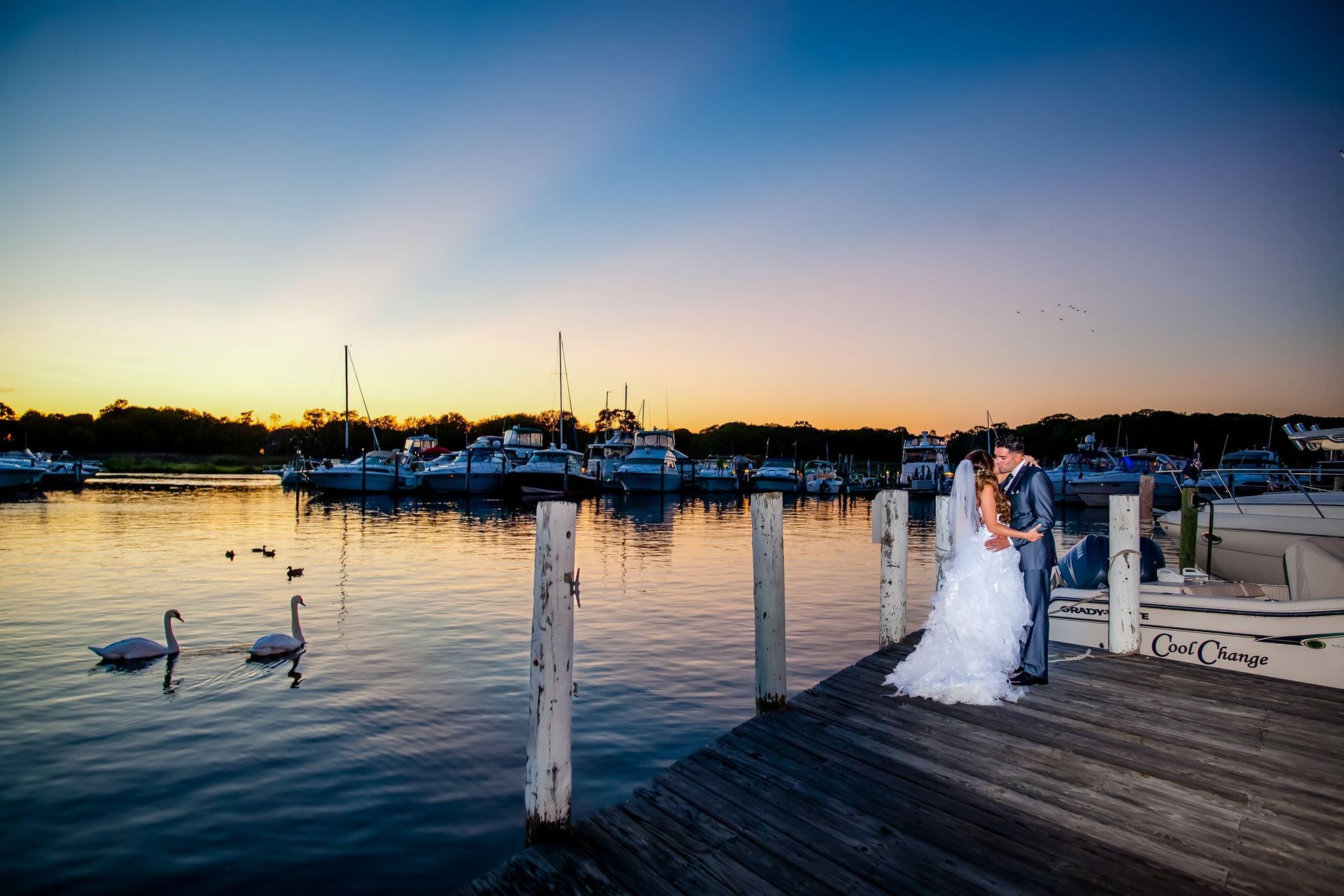 Newlyweds standing together beside a marina at dusk