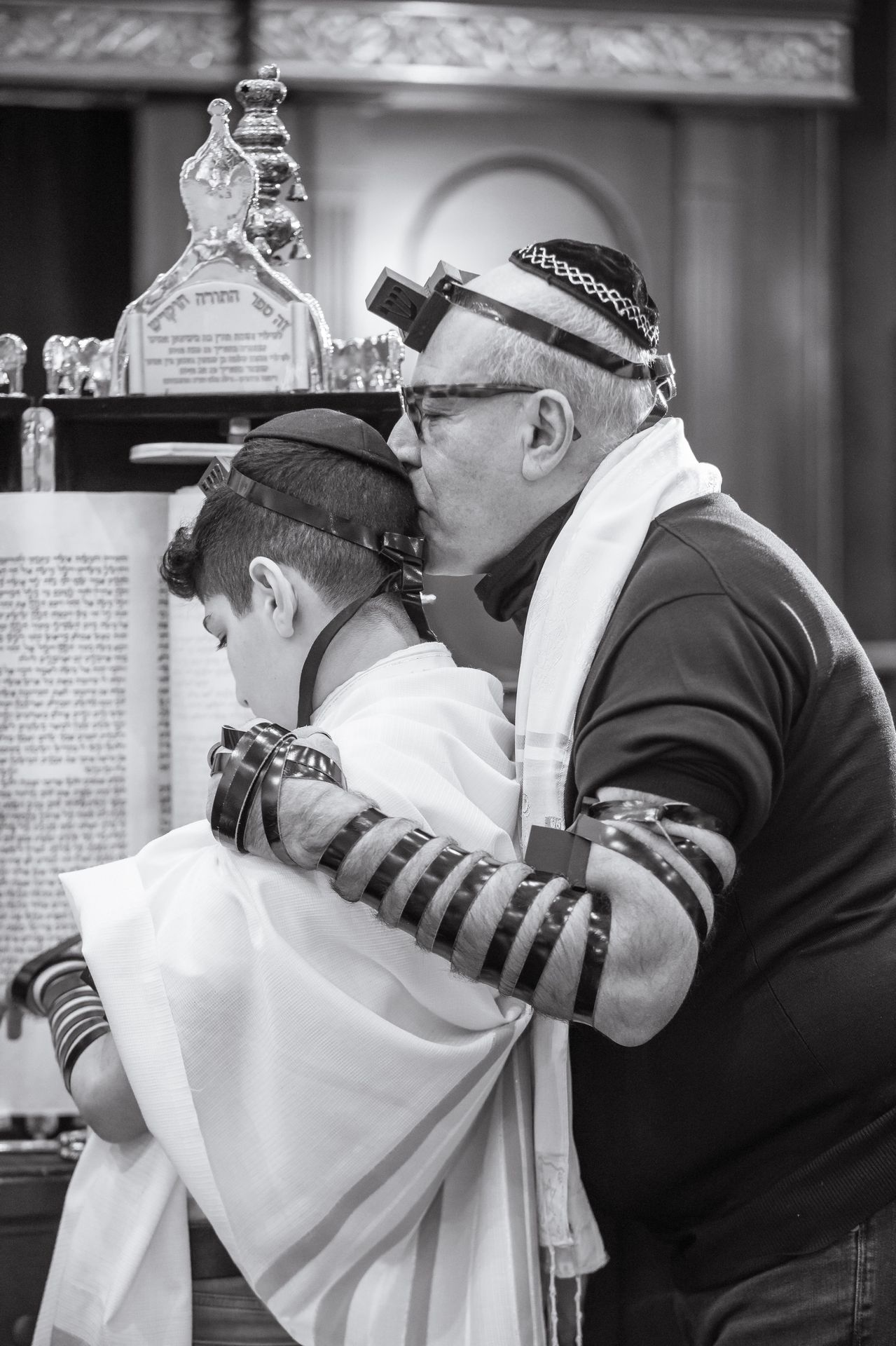 Black-and-white portrait of a father and his bar mitzvah son wearing tefillin at the Torah