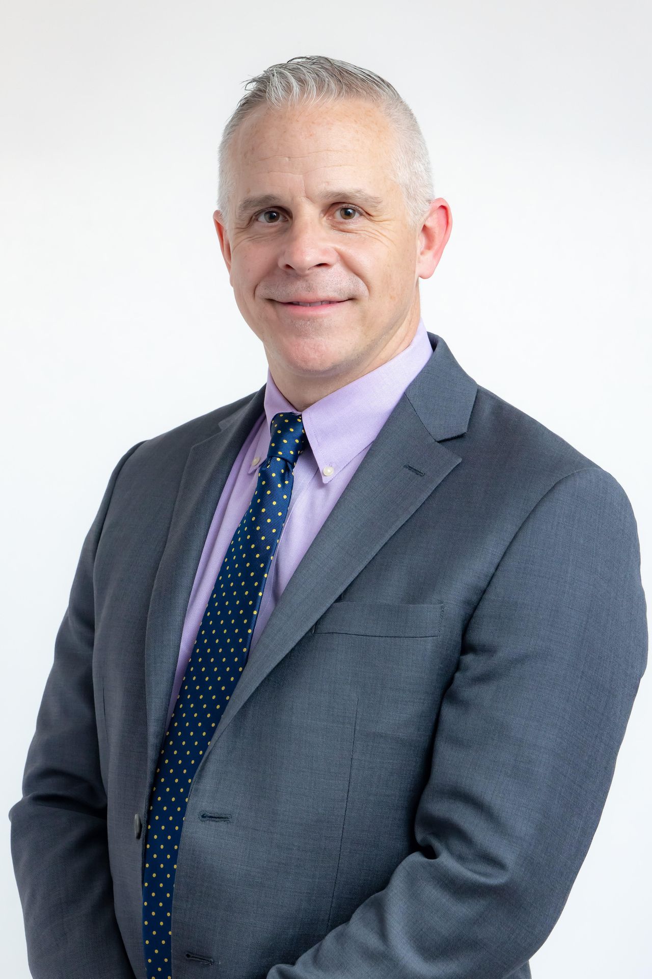 Smiling man in a gray suit, pink shirt and navy polka-dot tie on a light background